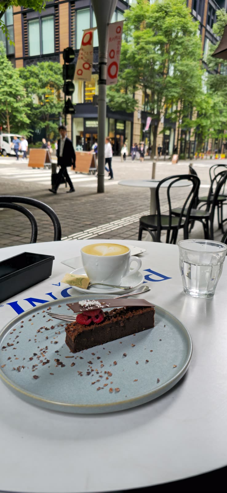 sidewalk cafe table with cappuccino and chocolate cake slice, European street behind
