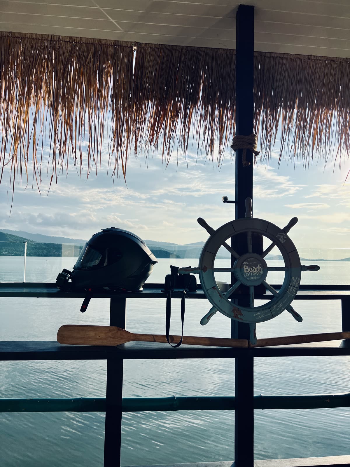 motorcycle helmet resting on a railing beside a decorative ship wheel and oar over water